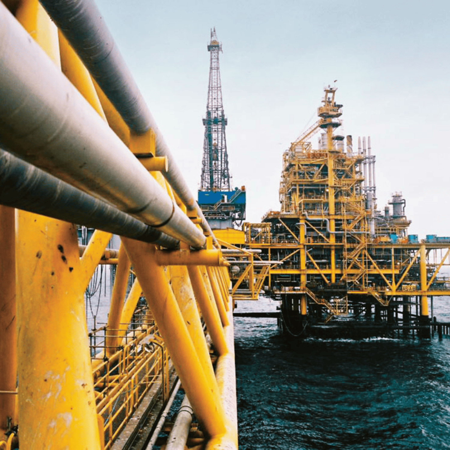 Oil rig platform with yellow structures and pipes in an offshore setting.